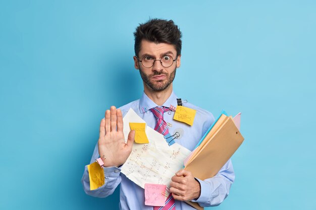 Empregado do sexo masculino espancado e sério diz segure puxa a palma da mão em direção à câmera em gesto de parar olha com expressão estrita recusa sua ajuda prepara o trabalho do projeto sozinho vestido formalmente