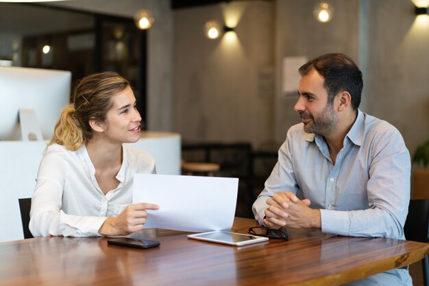 Empregado novo positivo que mostra o relatório ao colega do negócio