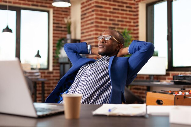 Empregado sentado com as mãos sobre a cabeça para relaxar depois de terminar o trabalho na mesa. Homem de negócios se sentindo calmo e tranquilo, relaxando no escritório depois de trabalhar no planejamento do projeto. Pessoa em pausa