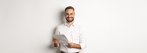 Empregador parecendo satisfeito com o trabalho lendo documentos e sorrindo satisfeito em pé sobre fundo branco