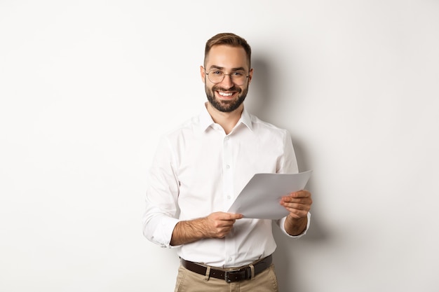 Foto grátis empregador parecendo satisfeito com o trabalho, lendo documentos e sorrindo satisfeito, em pé