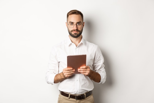 Foto grátis empregador sério trabalhando com tablet digital, lendo de óculos, em pé