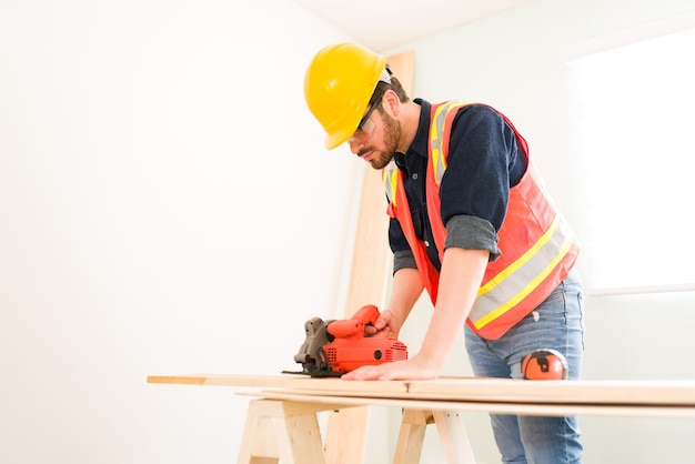 Foto grátis empreiteiro profissional masculino usando uma máquina de corte para cortar um painel de madeira no canteiro de obras