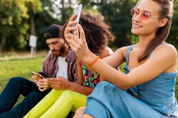 Empresa jovem e elegante e colorida de amigos sentados no parque, homens e mulheres se divertindo juntos