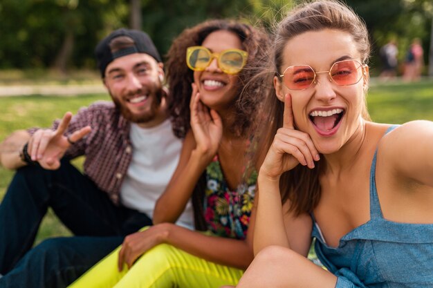 Empresa jovem e elegante e colorida de amigos sentados no parque, homens e mulheres se divertindo juntos