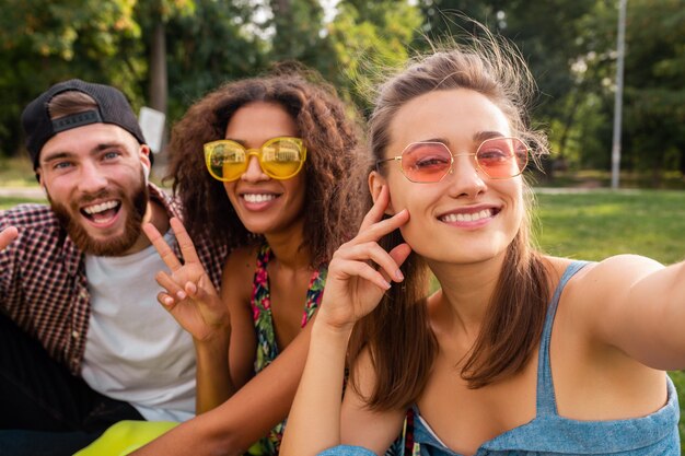 Empresa jovem e elegante e colorida de amigos sentados no parque, homens e mulheres se divertindo juntos