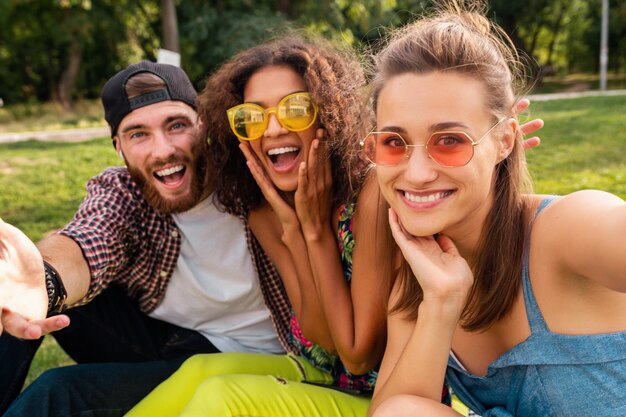 Empresa jovem e elegante e colorida de amigos sentados no parque, homens e mulheres se divertindo juntos