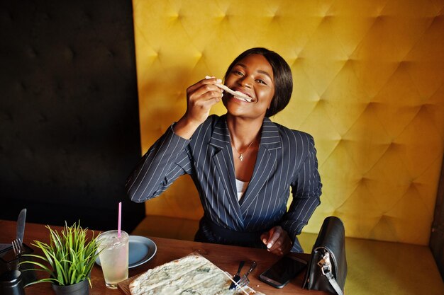 Empresária afro-americana comendo pizza de queijo no café Garota negra descansando