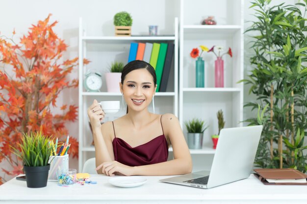 Empresária asiática fazer uma pausa para o café depois de trabalhar no computador portátil na mesa