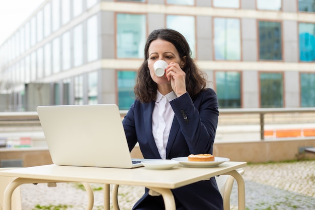 Empresária, bebendo café e usando o laptop