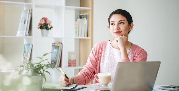 Empresária confiante, sorrindo e pensando, sentado no escritório moderno.