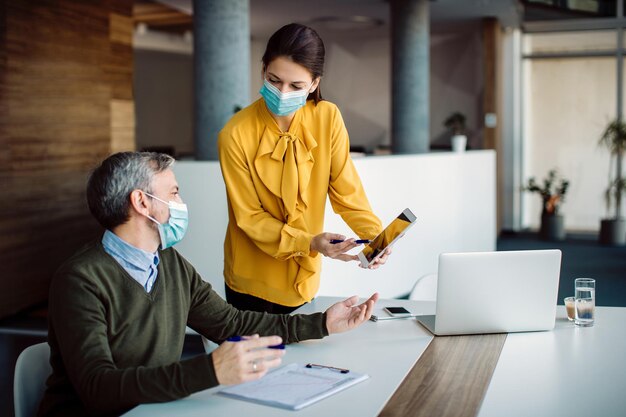 Empresária e seu colega conversando enquanto usam o touchpad no escritório e usam máscaras faciais