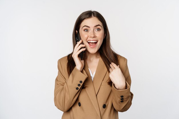 Empresária entusiasmada falando no celular, reagindo espantada e feliz em ligar, receber ótimas notícias, de pé sobre fundo branco