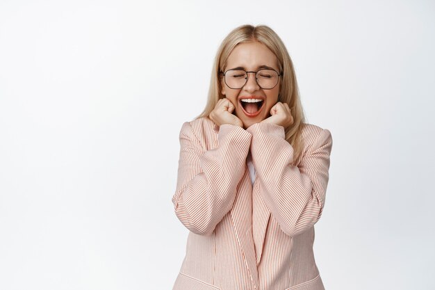 Empresária gritando de espanto, reagindo de surpresa e animada com uma grande notícia, de terno e óculos branco.