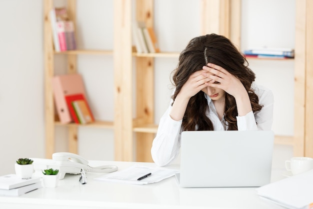 Empresária jovem cansada, sofrendo muito tempo sentado na mesa do computador no escritório