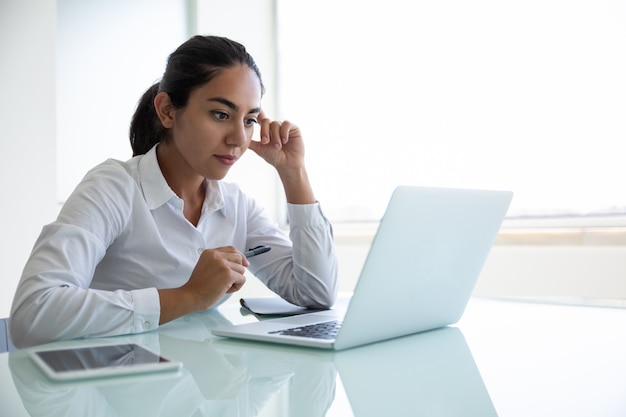 Empresária jovem concentrada usando laptop no escritório