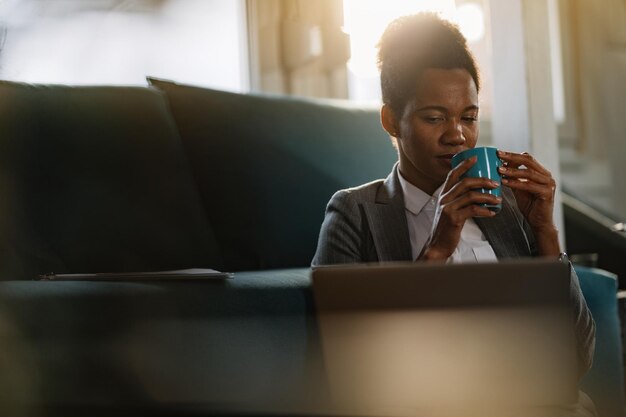 Empresária negra pensativa lendo um e-mail no laptop enquanto toma café em casa
