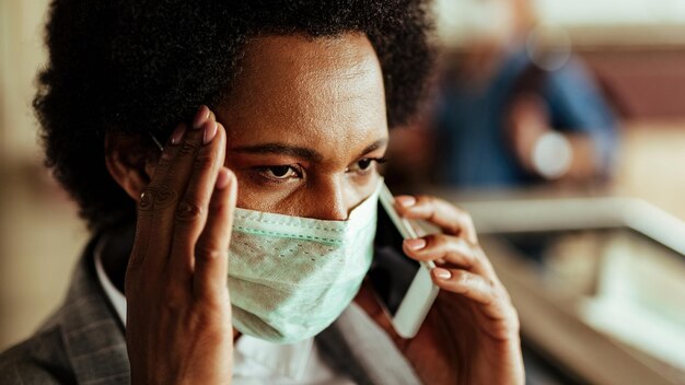 Empresária negra perturbada se comunicando por telefone celular enquanto usava máscara protetora durante epidemia de vírus