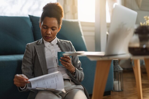 Empresária negra tomando café e analisando relatórios de negócios enquanto trabalhava em casa