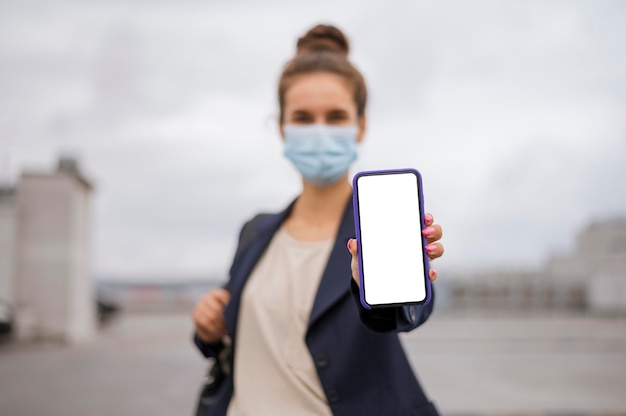 Foto grátis empresária segurando um smartphone em branco enquanto usa uma máscara médica