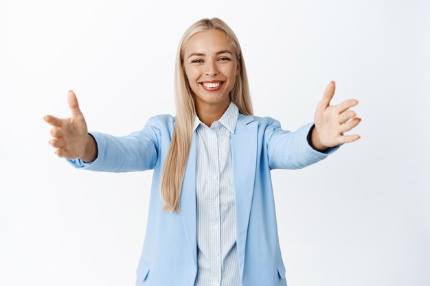 Empresária sorridente de terno azul esticando as mãos para dar boas-vindas ao abraço recebe algo de pé sobre fundo branco