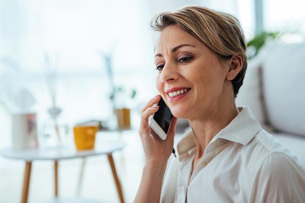 Empresária sorridente usando telefone inteligente enquanto conversa com alguém em casa