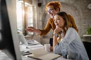 Foto grátis empresárias felizes lendo um e-mail no computador enquanto trabalham juntas no escritório o foco está na mulher ruiva