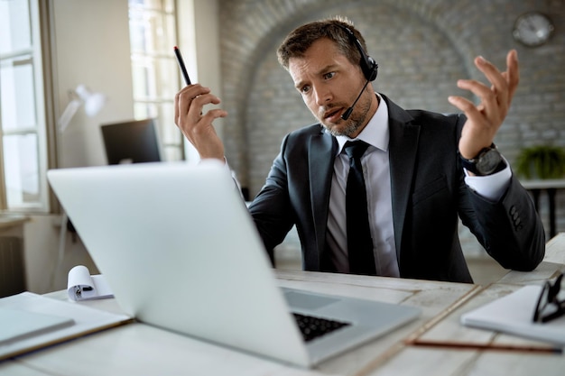 Empresário adulto médio usando laptop enquanto tem reunião on-line no escritório