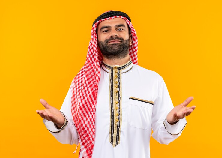 Foto grátis empresário árabe com roupa tradicional e sorriso confiante, levantando os braços em pé sobre a parede laranja