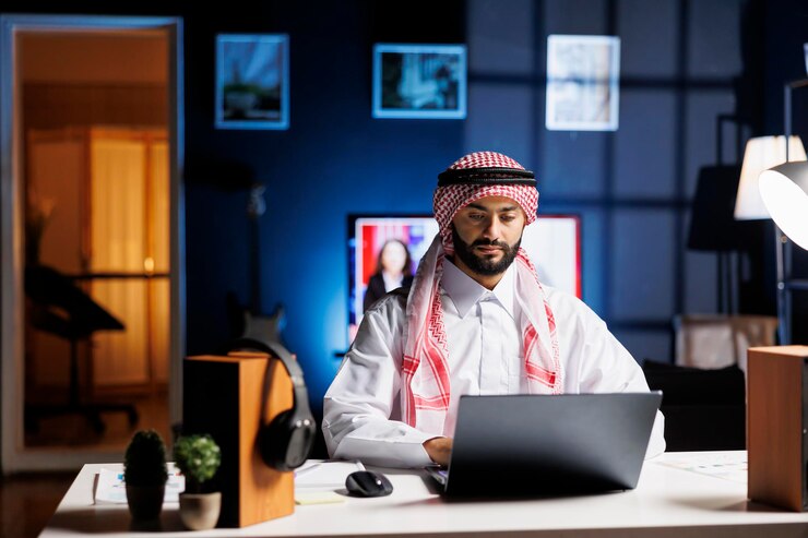 Foto grátis empresário árabe confiante trabalhando em uma mesa moderna, digitando em seu laptop. homem muçulmano envolvido em navegação, comunicação por e-mail e conectividade sem fio em um ambiente de escritório calmo e profissional.