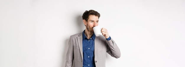 Empresário bonito de terno bebendo café ou chá da caneca do escritório olhando de lado para o logotipo em pé