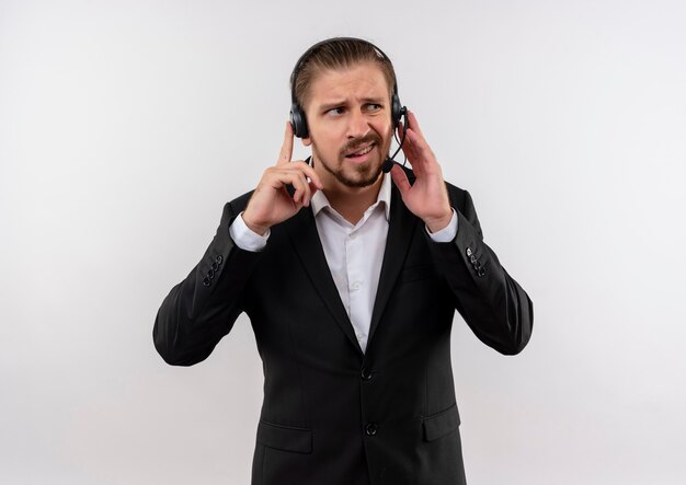 Empresário bonito de terno e fones de ouvido com um microfone ouvindo um cliente parecendo confuso em pé sobre um fundo branco