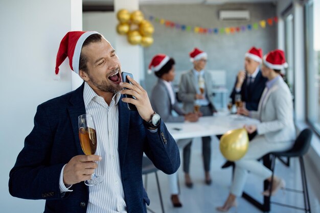 Empresário brincalhão assinando enquanto estiver usando telefone inteligente na festa de Natal no escritório