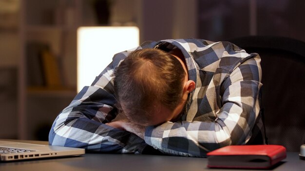 Empresário cansado, dormindo com a cabeça na mesa do escritório em casa. Empreendedor com excesso de trabalho.