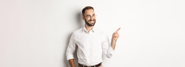 Foto grátis empresário confiante parecendo satisfeito e apontando o dedo para a esquerda mostrando o banner da empresa em pé