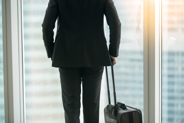 Foto grátis empresário de pé com mala perto da janela