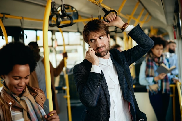 Empresário descontente fazendo um telefonema enquanto se desloca para o trabalho de ônibus