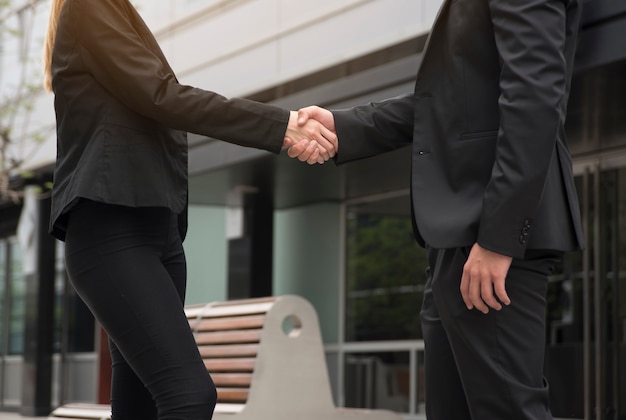 Empresário e empresária estão apertando as mãos na frente do prédio de escritórios