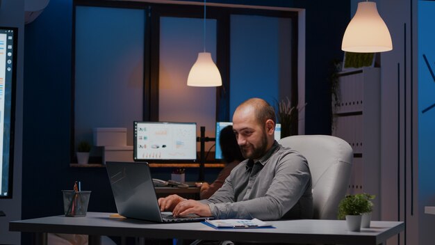 Empresário exausto, verificando estatísticas de marketing em um laptop, trabalhando no escritório de uma empresa iniciante