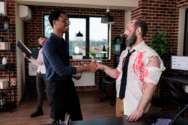 Foto grátis empresário fazendo aperto de mão com zumbi malvado, conversando com cérebro comendo cadáver no escritório de inicialização. monstro assustador morto-vivo com feridas sangrentas saudando pessoa, diabo sinistro.