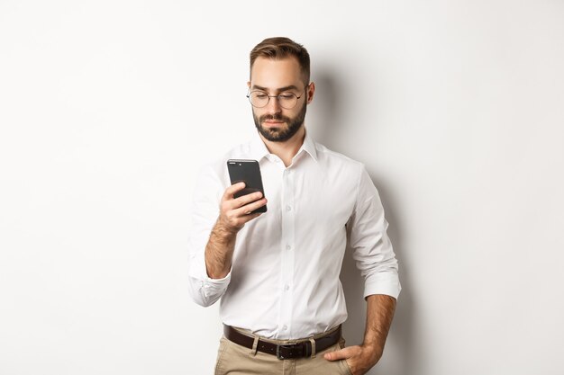 Empresário lendo mensagem no telefone, em pé.