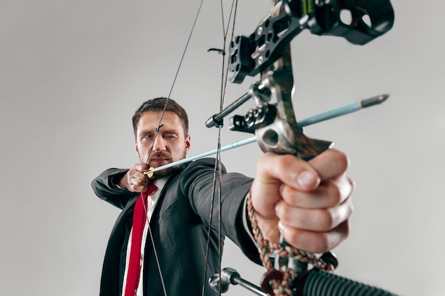 Empresário mirando no alvo com arco e flecha, isolado no fundo branco