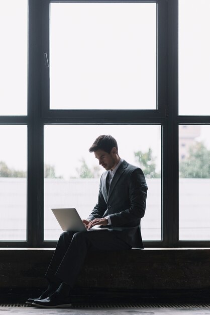 Empresário moderno com laptop no colo, sentado em frente a janela