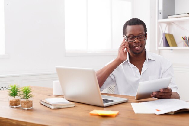 Empresário negro com papéis e celular. jovem discutindo documentos no celular em um escritório moderno, copie o espaço