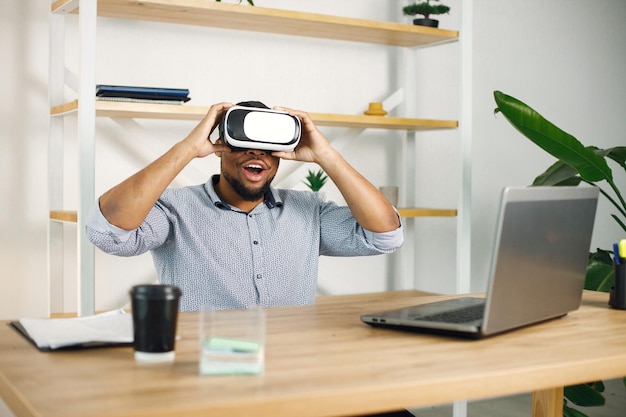 Foto grátis empresário negro sentado no escritório e usando óculos de realidade virtual