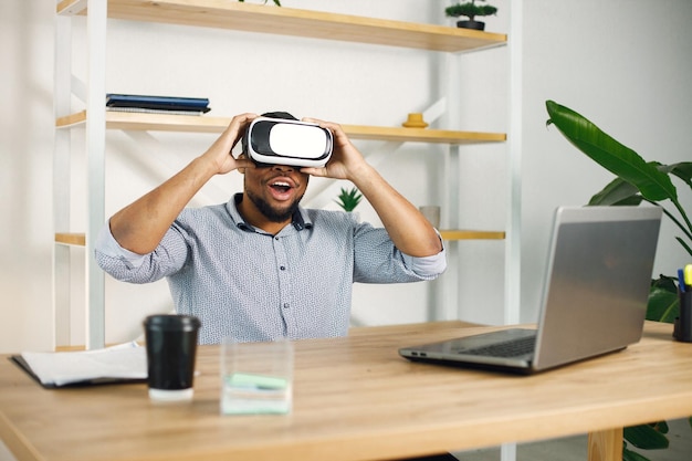 Empresário negro sentado no escritório e usando óculos de realidade virtual