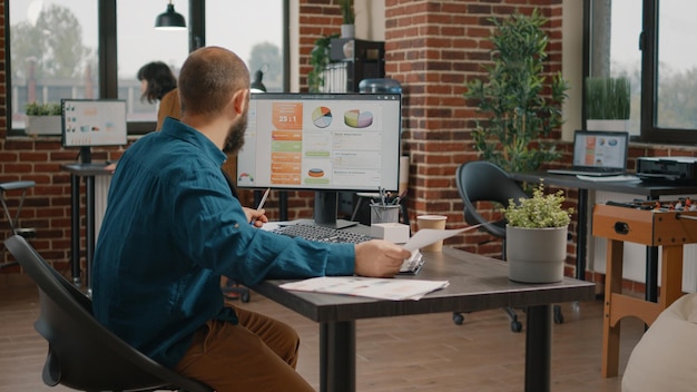 Foto grátis empresário olhando para papéis e computador com gráficos de taxas para planejar o projeto para apresentação. homem de negócios trabalhando com análise de dados e informações para criar estratégia de marketing.