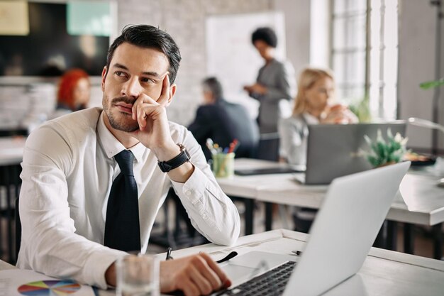 Empresário pensativo sentado à mesa no escritório e pensando em novas ideias Há pessoas em segundo plano