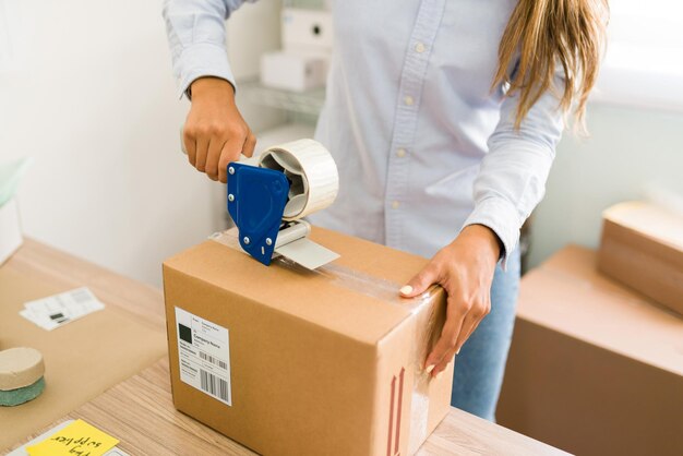 Empresário pronto para enviar os pedidos de seus clientes. Feche as mãos femininas colocando fita em um grande pacote com produtos