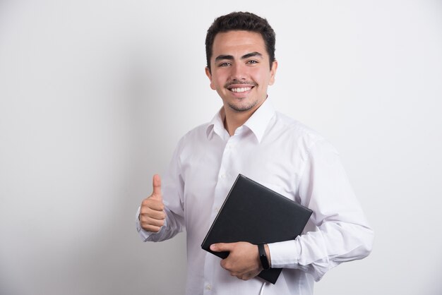 Empresário segurando laptop e mostrando os polegares em fundo branco.